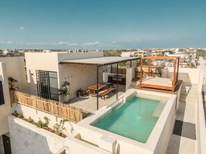 Ein Pool auf dem Dach mit Holzterrasse, einer überdachten Sitzgelegenheit und Blick auf die Stadt.