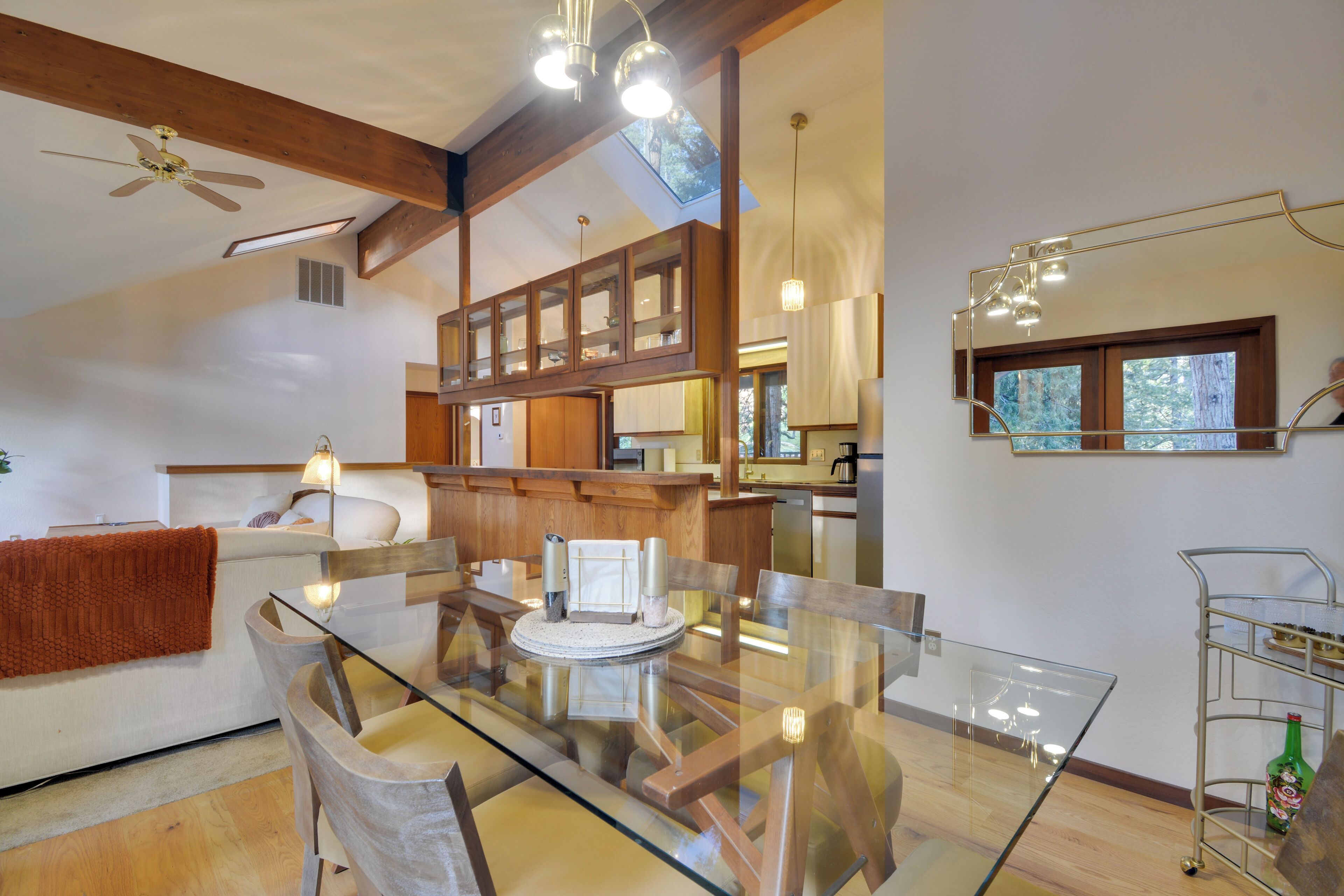 A modern kitchen with wooden cabinets, a glass dining table, and a ceiling fan.