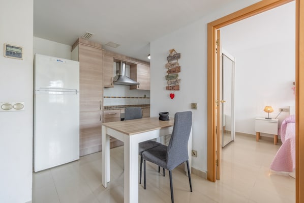 Una cocina compacta con refrigerador, armarios de madera, una mesa de comedor con dos sillas y una pared decorada con letreros motivacionales.