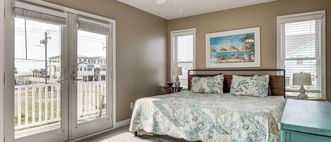 A bedroom with a bed, a ceiling fan, a painting, and a view through the sliding glass doors.