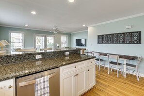 A kitchen with granite countertops, white cabinetry, a ceiling fan, and a dining area with a wooden table and chairs.
