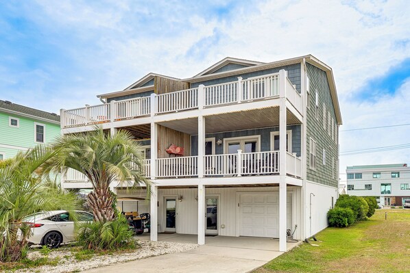 A two-story building with a balcony, a garage, and a small front yard with a palm tree.