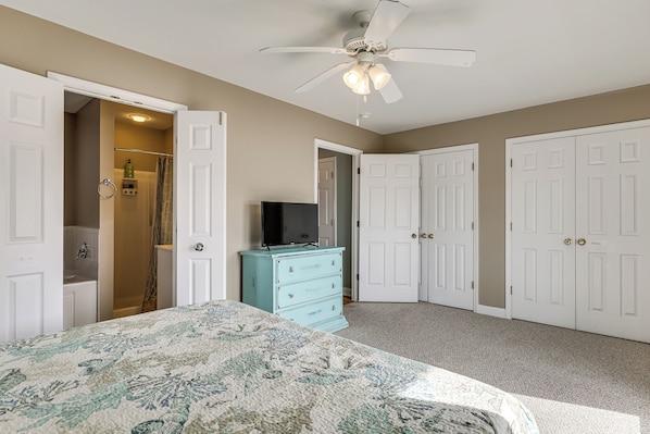 A bedroom with a bed, a dresser, a ceiling fan, and a TV.