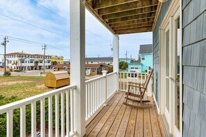 A wooden porch with a rocking chair, a white railing, and a view of neighboring houses.