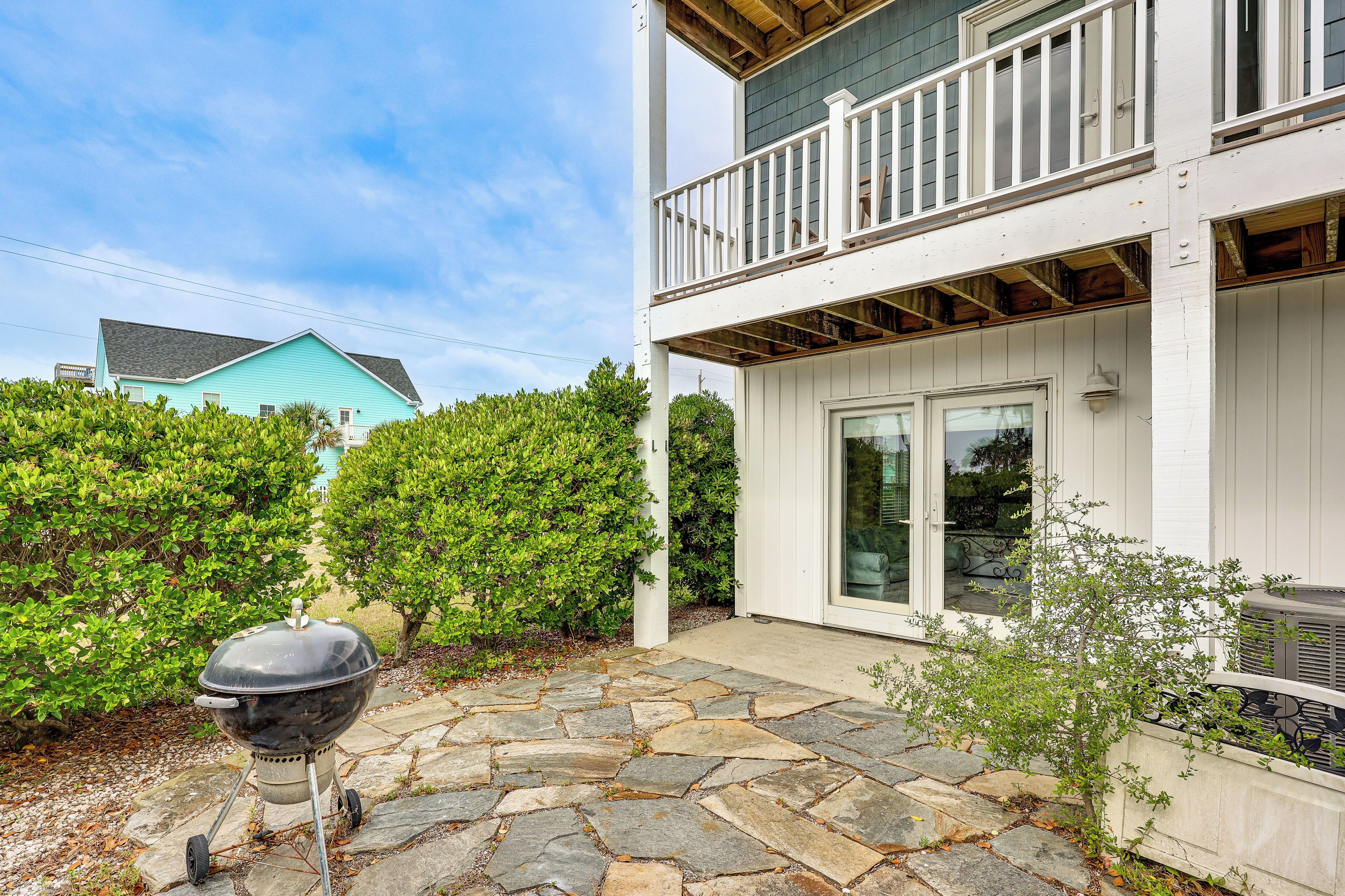 A two-story house with a stone patio, a barbecue grill, and a white balcony.