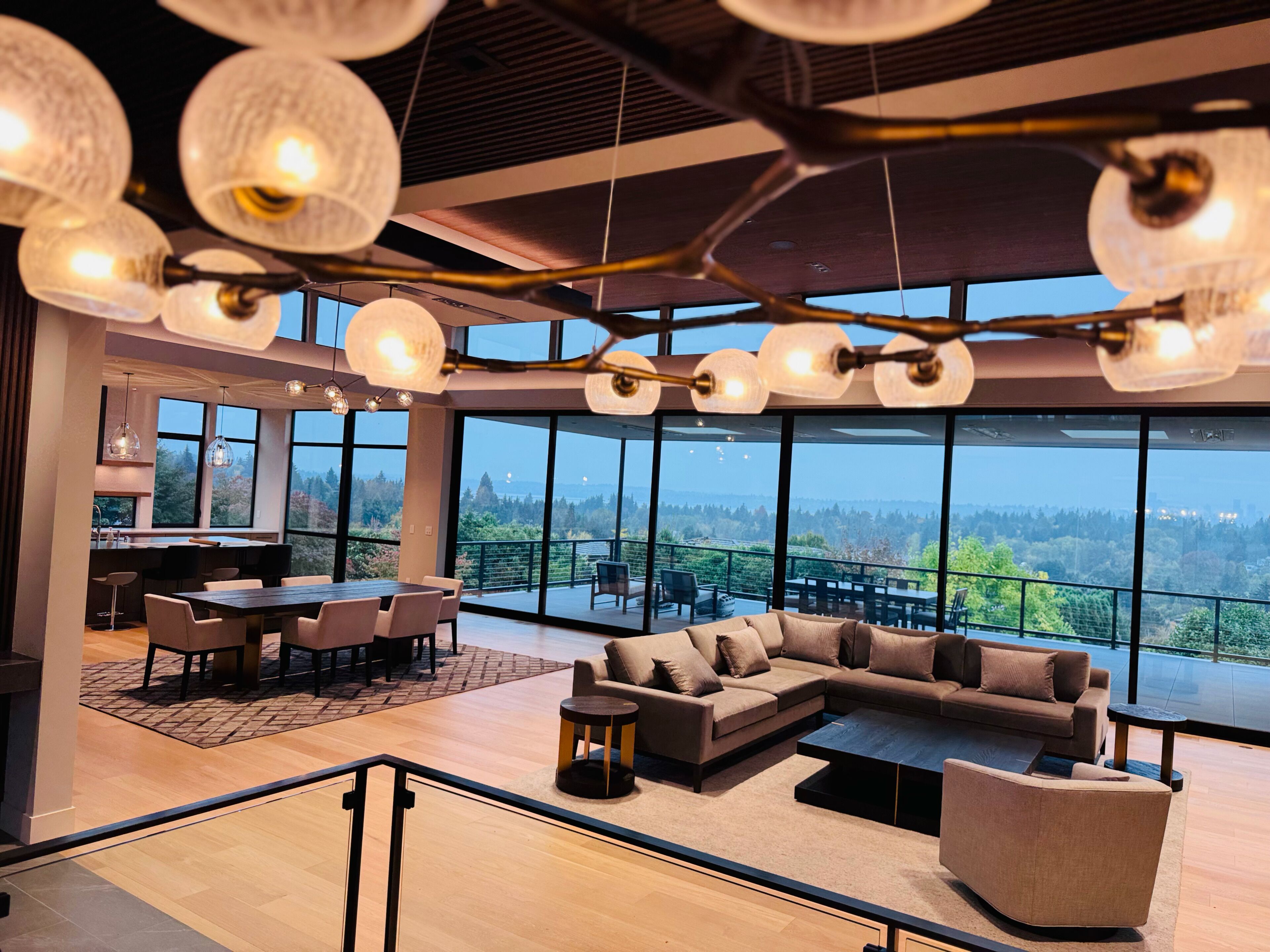 Un interior moderno con comedor, sofá y grandes ventanales que ofrecen vistas al exterior.