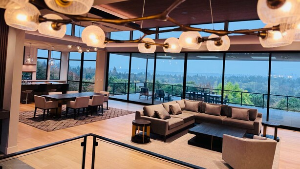 Un interior moderno con comedor, sofá y grandes ventanales que ofrecen vistas al exterior.
