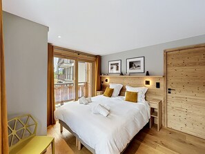 Ein Schlafzimmer mit einem Bett, einem hölzernen Kopfteil, zwei Nachttischen, einem Sessel und einem großen Fenster mit Blick.