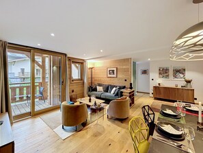 Ein großzügiger Wohnbereich mit Sofa, Couchtisch und Sesseln, ein Essbereich mit Tisch für zwei Personen sowie ein Balkon mit Blick.