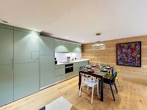 Eine moderne Küche mit grünen Schränken, eine Essecke mit Holztisch und ein farbenfrohes abstraktes Gemälde an der Wand.
