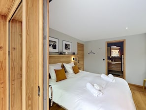 Ein Schlafzimmer mit einem hölzernen Kopfende, einem Bett mit weißer Bettwäsche, zwei gerollten Handtüchern, einem Holzschrank und einem Spiegel.