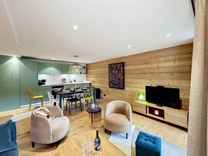 Ein modernes Wohnzimmer mit einer Couch, Sesseln, einem Esstisch und einem Fernseher.