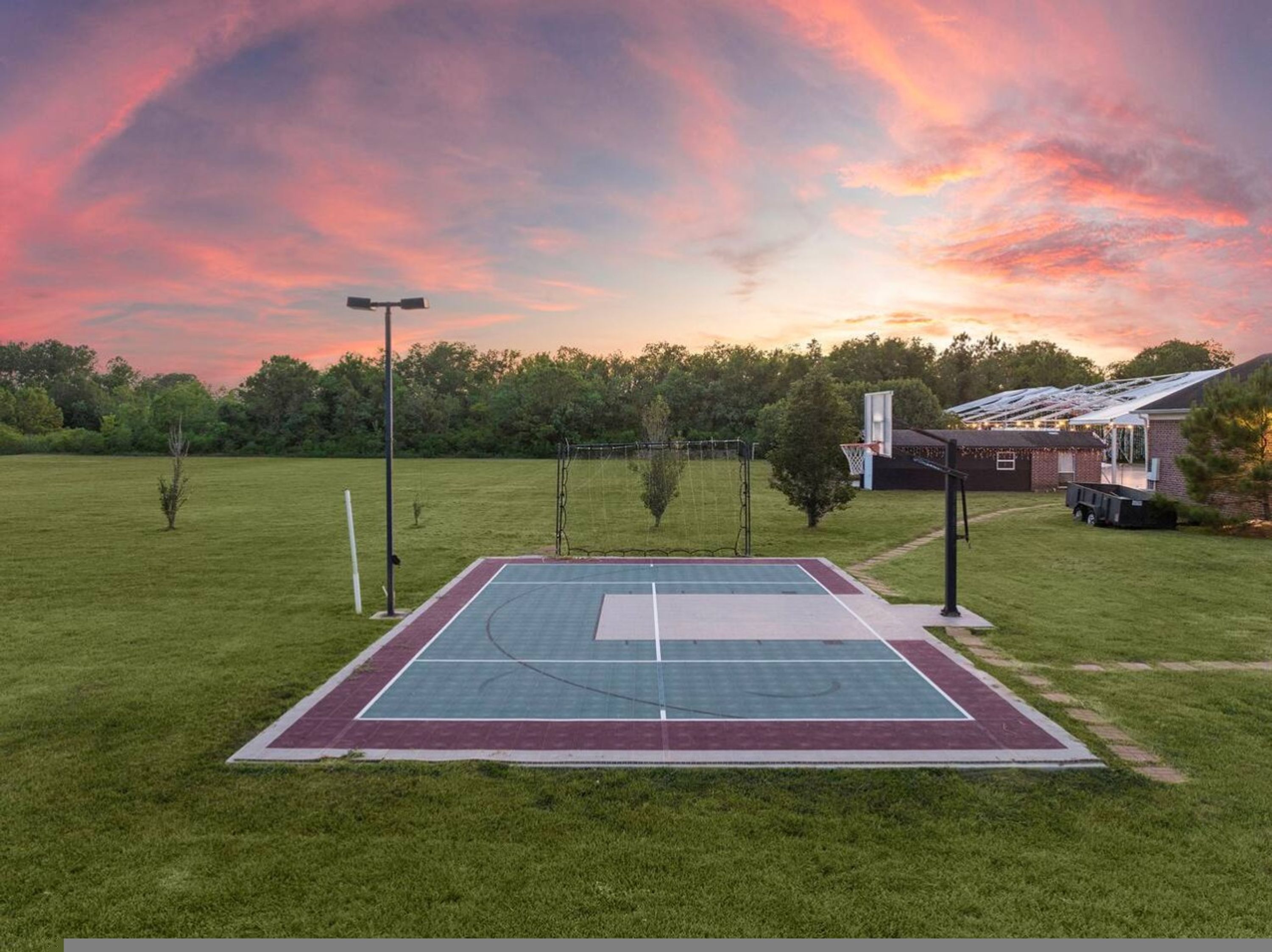An outdoor basketball court with a net, a goal, and a fence.