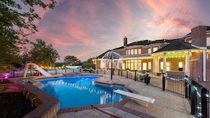A swimming pool with a slide, surrounded by a brick building with a covered patio area. - Private Mansion Retreat Basketball Court and More (Dickinson)