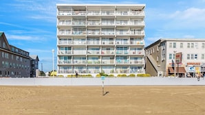 Ein mehrstöckiges Hotel mit Balkonen, feinem Sand vor der Fassade und blauem, wolkenlosem Himmel.
