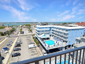 Ein mehrstöckiges Hotel mit Pool, Parkplatz und Blick auf das Meer.