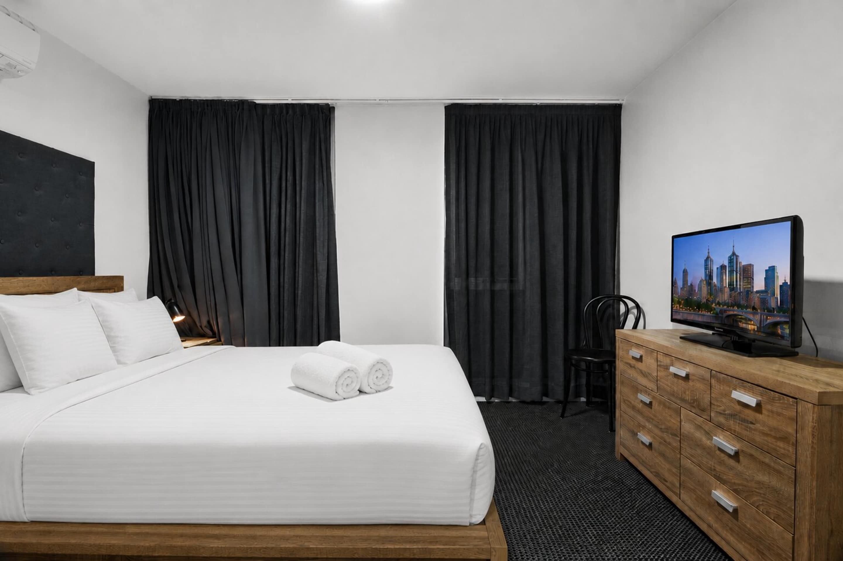 Une chambre d’hôtel avec un lit, une télévision, une commode en bois et une vue sur la ville.