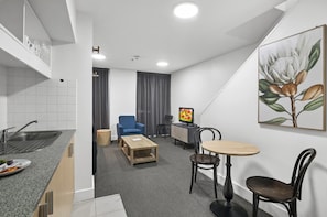 Ein kompaktes Hotelzimmer mit Küchenzeile, Essbereich, Sitzecke mit Fernseher und einem Bild an der Wand.