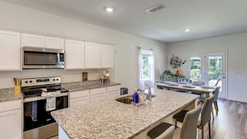 A modern kitchen with white cabinetry, a granite countertop, stainless steel appliances, and a dining area with a large island.