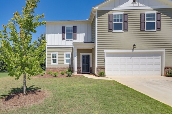 A two-story house with a garage, a front door, and a small tree in the yard.