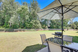 An outdoor patio with a table and chairs, a grill, and a large umbrella.