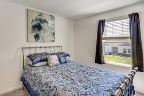 A bedroom with a bed, a window with curtains, a wall-mounted abstract painting, and a metal headboard.