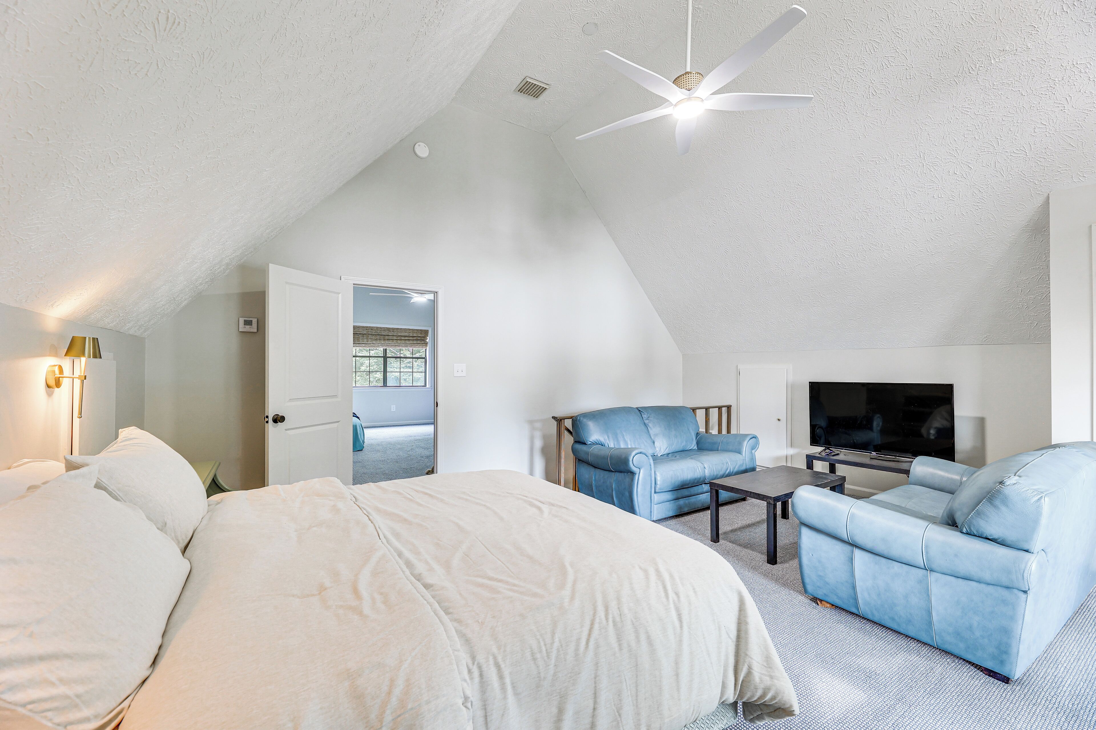 A bedroom with a bed, a blue armchair, a sofa, a TV, and a ceiling fan.