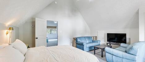 A bedroom with a bed, a blue armchair, a sofa, a TV, and a ceiling fan.