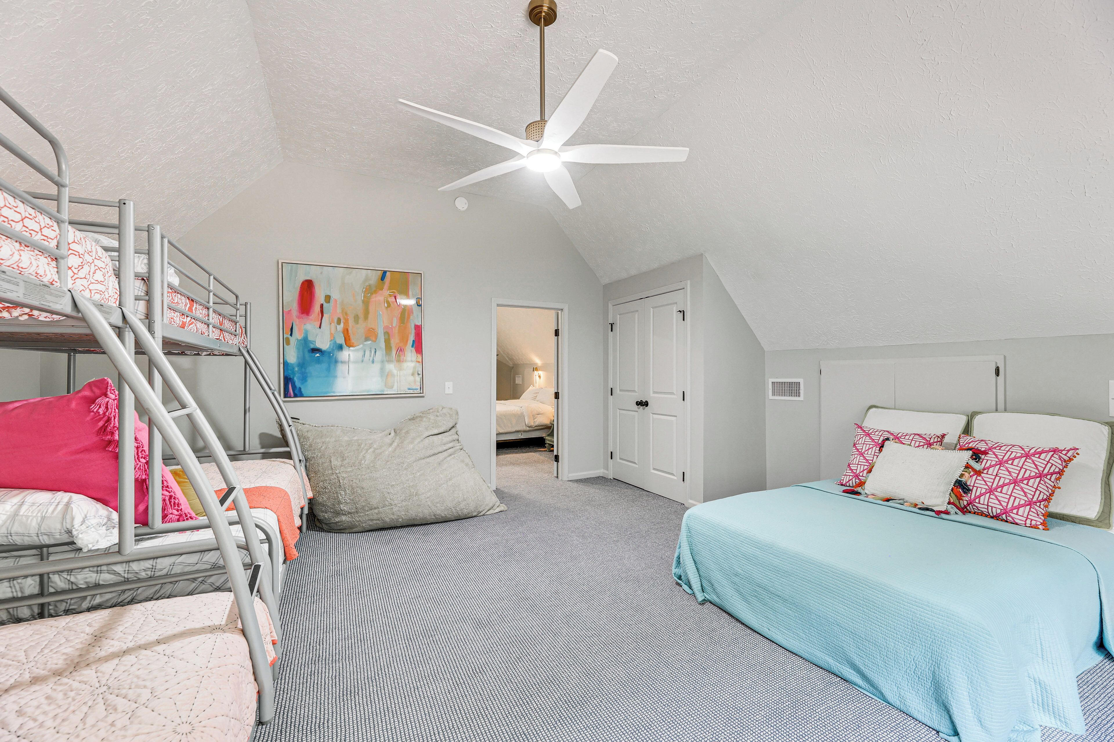 Une chambre avec des lits superposés, un ventilateur de plafond, un tableau et une porte donnant sur une autre pièce.