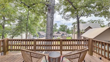 A wooden deck with wicker chairs and a table, overlooking a residential area with houses and parked cars.