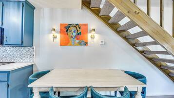 Un comedor con mesa de madera y sillas tapizadas en azul, un cuadro en la pared y una escalera con barandillas de madera.