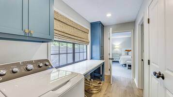 A laundry area with a washing machine, a bench, and a window with blinds.