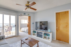 A room with a TV, a wooden door, a balcony with a chair, and a bed with a view. - Bayfront Condo w/ Sunset Views! Walk to Beach (Seaside Heights)