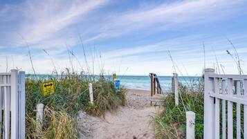 Ein Pfad am Sandstrand mit einer Holzbank und einem weißen Zaun.