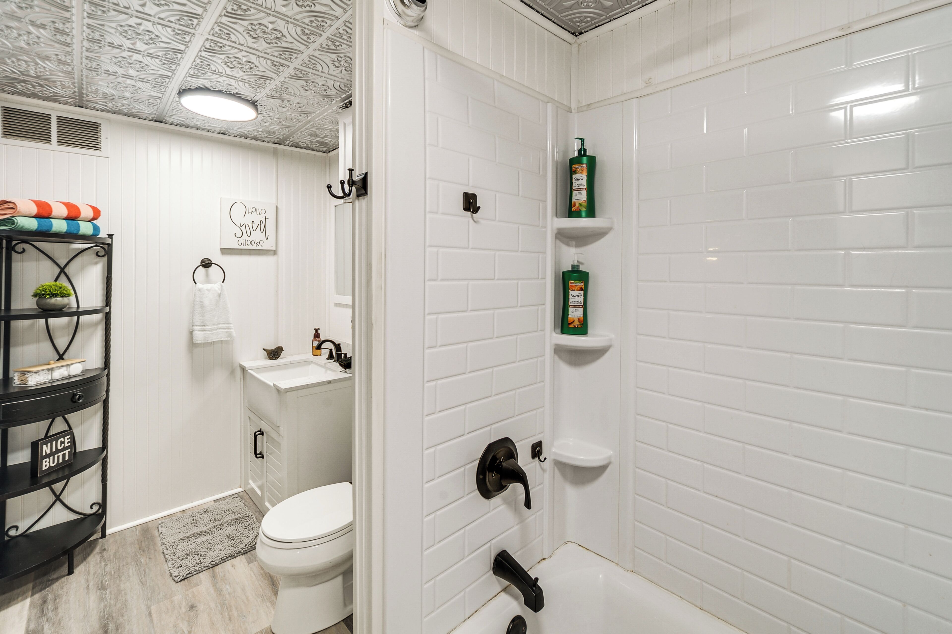 A bathroom with white subway tiles, a white toilet, a black shelf with toiletries, and a shower area with a white tiled wall.