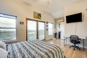 Ein Schlafzimmer mit Bett, Schreibtisch, Stuhl, Fernseher, Ventilator und Blick ins Freie.