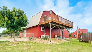 A red barn with a wooden deck, surrounded by a fenced yard and trees. - Fredericksburg Barn w/ Balcony: Sip, Soak + Hike (Fredericksburg)