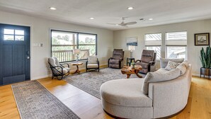 Ein geräumiges Wohnzimmer mit großem Fenster, Deckenventilator und grauem, rundem Sofa.