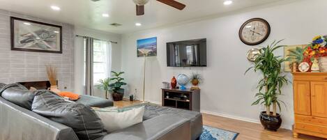 A modern living room with a leather sofa, a ceiling fan, a flat-screen TV, a wooden cabinet, and potted plants.