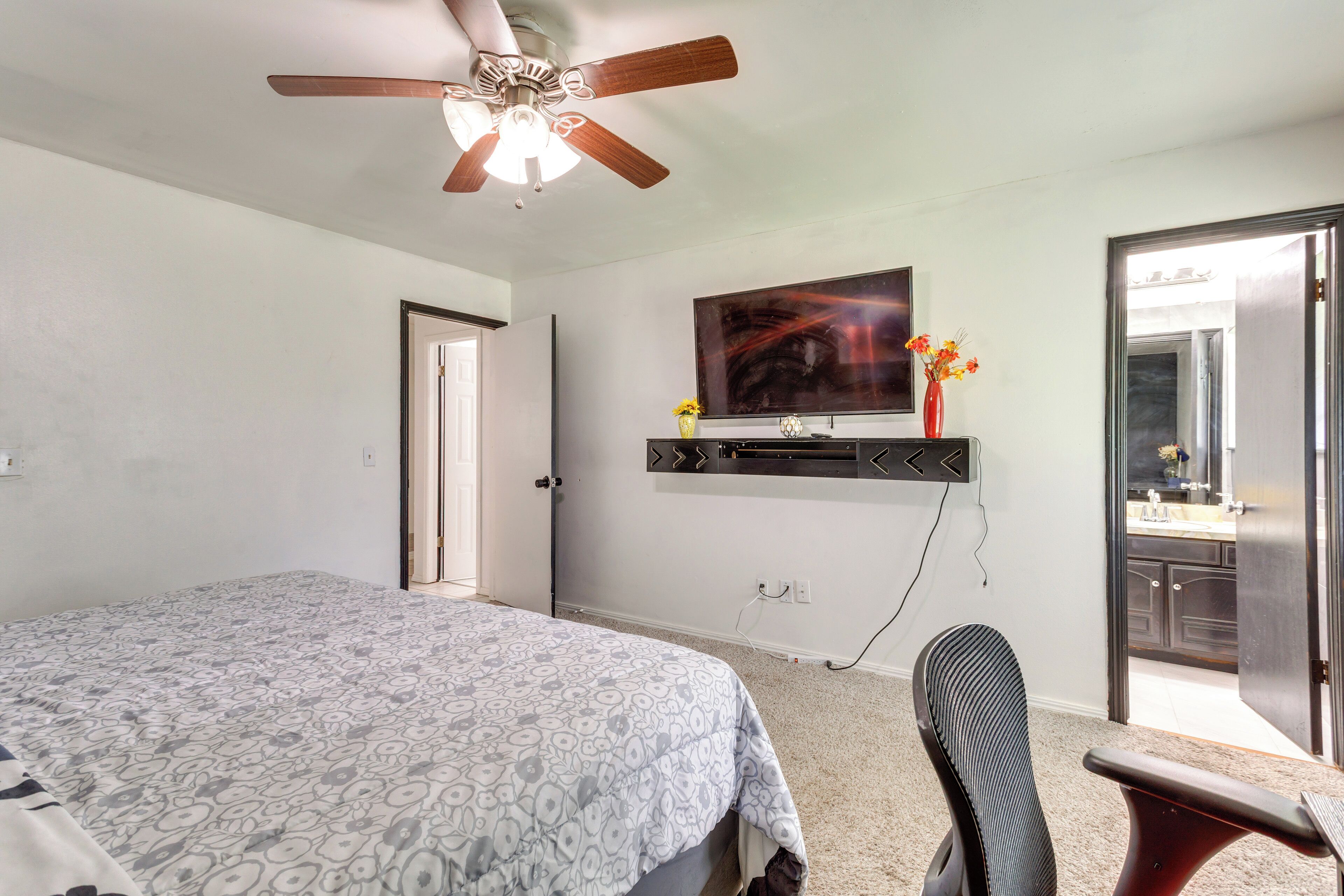 Une chambre à coucher comprenant un lit, un ventilateur de plafond, un téléviseur fixé au mur et une porte donnant sur une salle de bain.