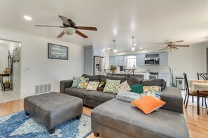 Ein modernes Wohnzimmer mit grauem Sofa, Hocker und Deckenventilatoren.