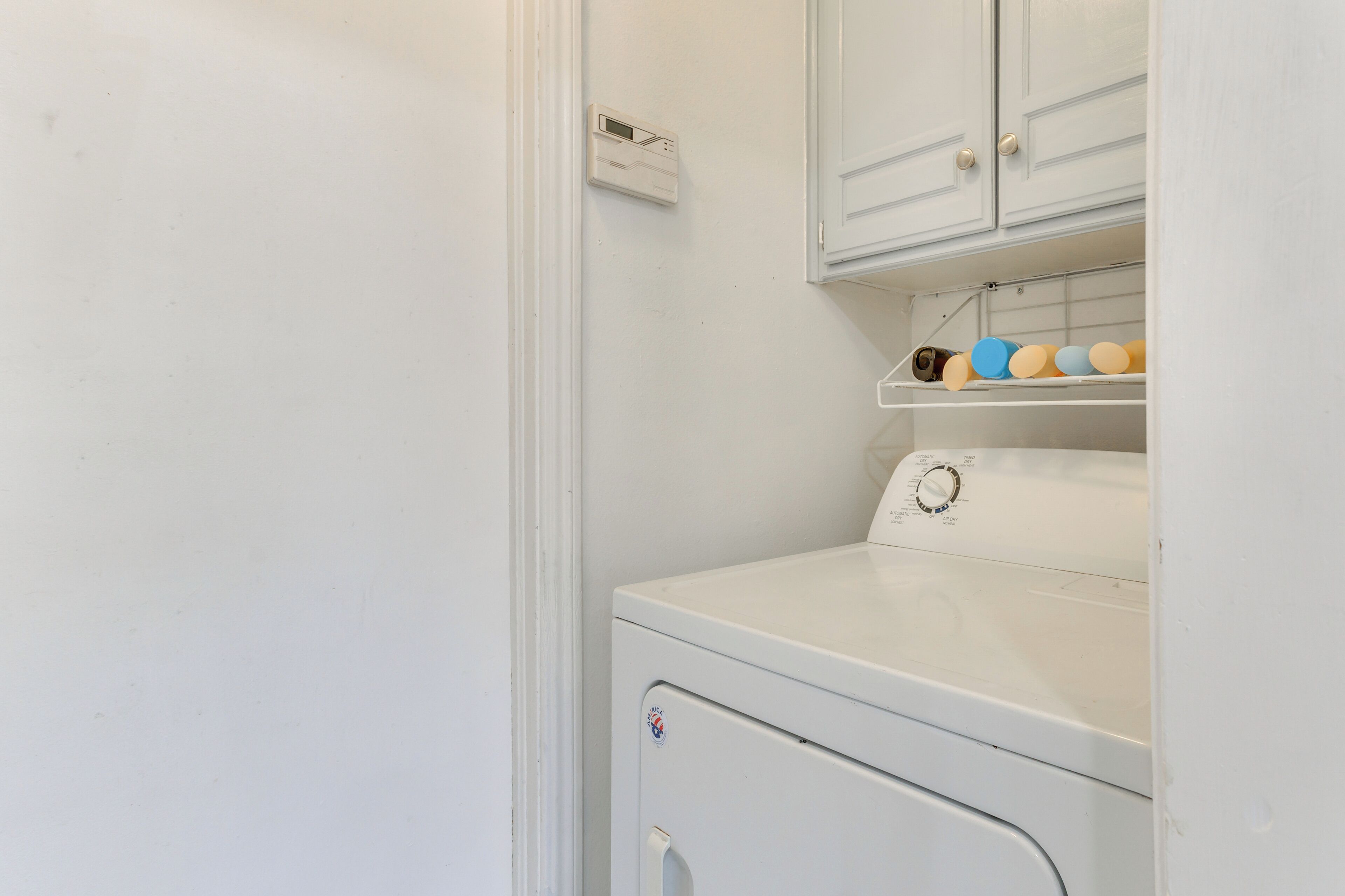 A laundry room with a white washing machine, a shelf with colorful laundry baskets, and a thermostat on the wall.
