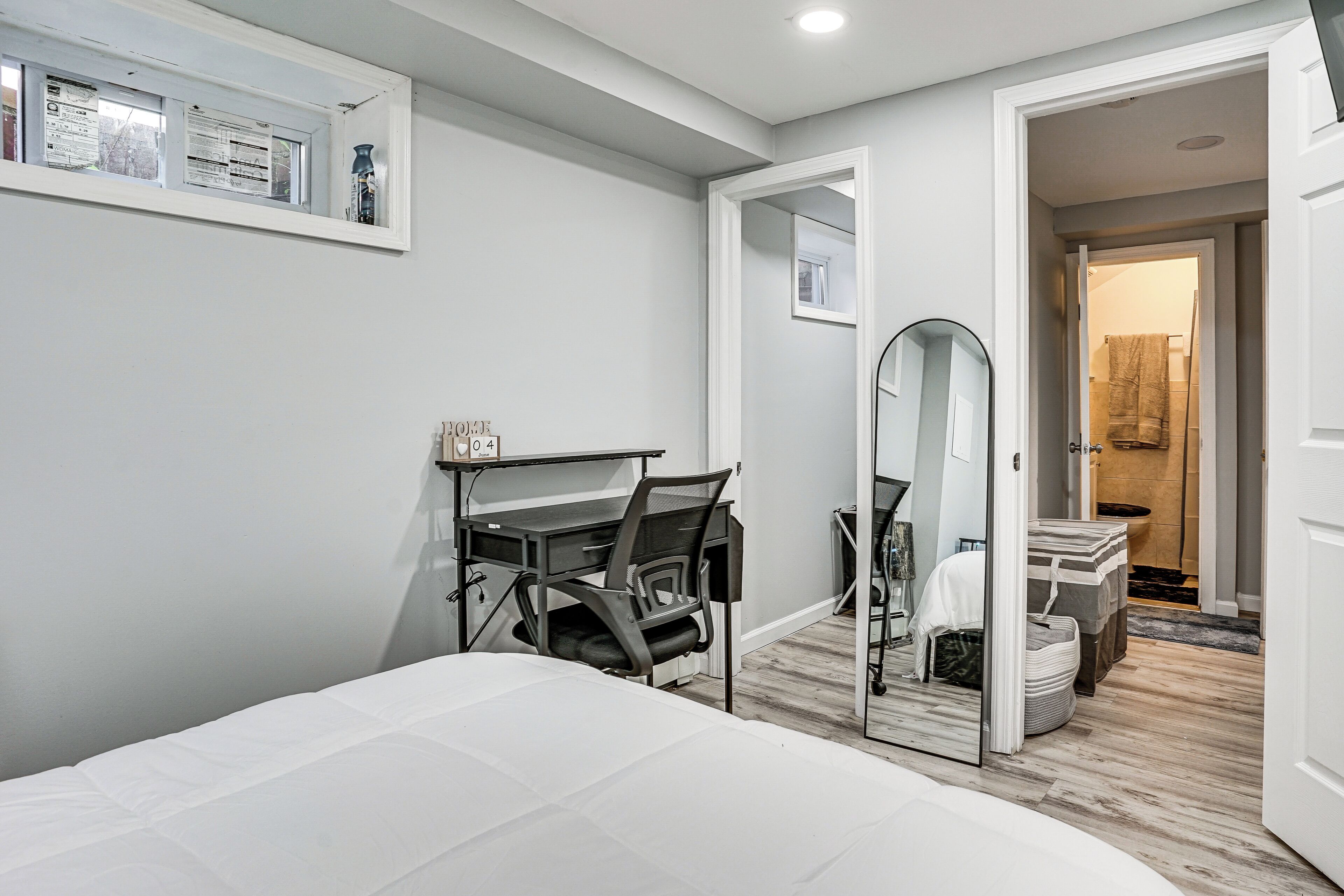 A bedroom with a bed, a desk, a chair, a mirror, and a door leading to another room.