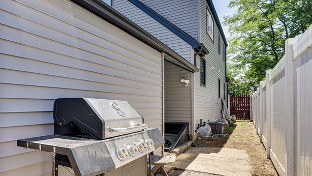 A backyard with a grill, a wooden deck, and a house with siding.