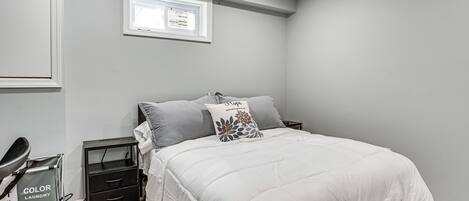 A bedroom with a bed, nightstand, and a small window.