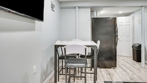 A modern kitchen with a white table, black chairs, a stainless steel refrigerator, and a white door.