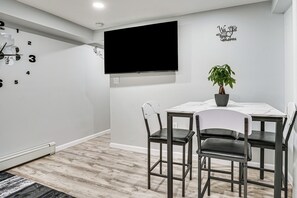 Una habitación moderna con televisión de pantalla plana, un reloj de pared, una planta en maceta y una mesa de comedor con sillas.
