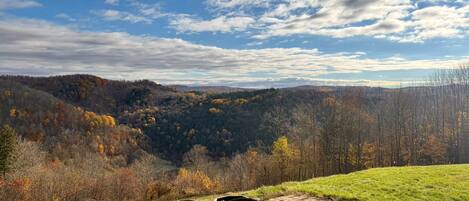 A paved outdoor seating area with two chairs and a table, overlooking a forested valley with autumn foliage.