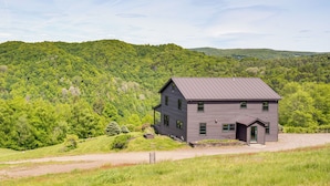 A two-story house with a metal roof, surrounded by lush green hills. - 95-acre Countryside Estate! Luxe Vermont Farmhouse (Chelsea)