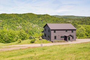 Une maison à deux étages, avec un toit en métal, entourée de collines verdoyantes.